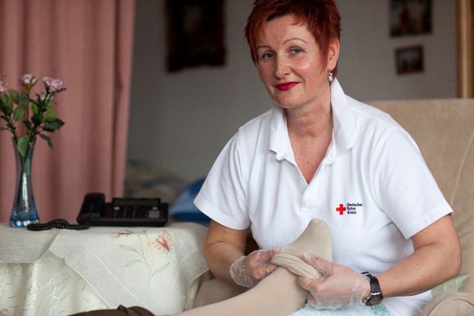 Ambulanter Pflegedienst des DRK Pflegekraft hilft einer Person beim Anziehen von Stützstrümpfen.